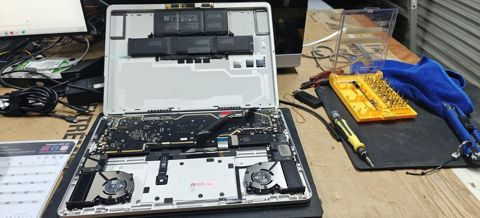 A laptop stripped down on the workbench with the repair toolkit beside it